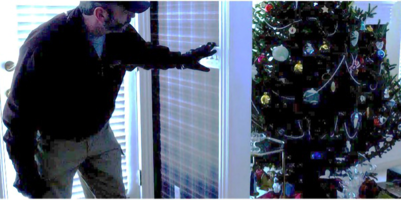 A burglar breaking into a home with a Christmas Tree in the background.