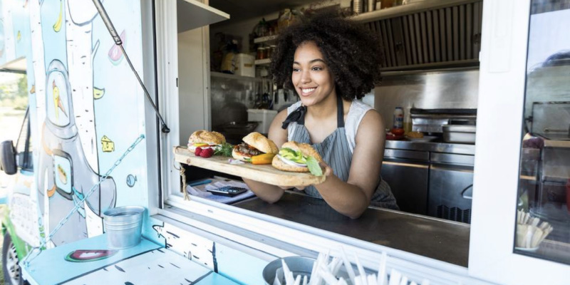 Smiling food truck owner serving gourmet sandwiches from a colorful mobile kitchen, representing food truck business insurance needs and coverage options
